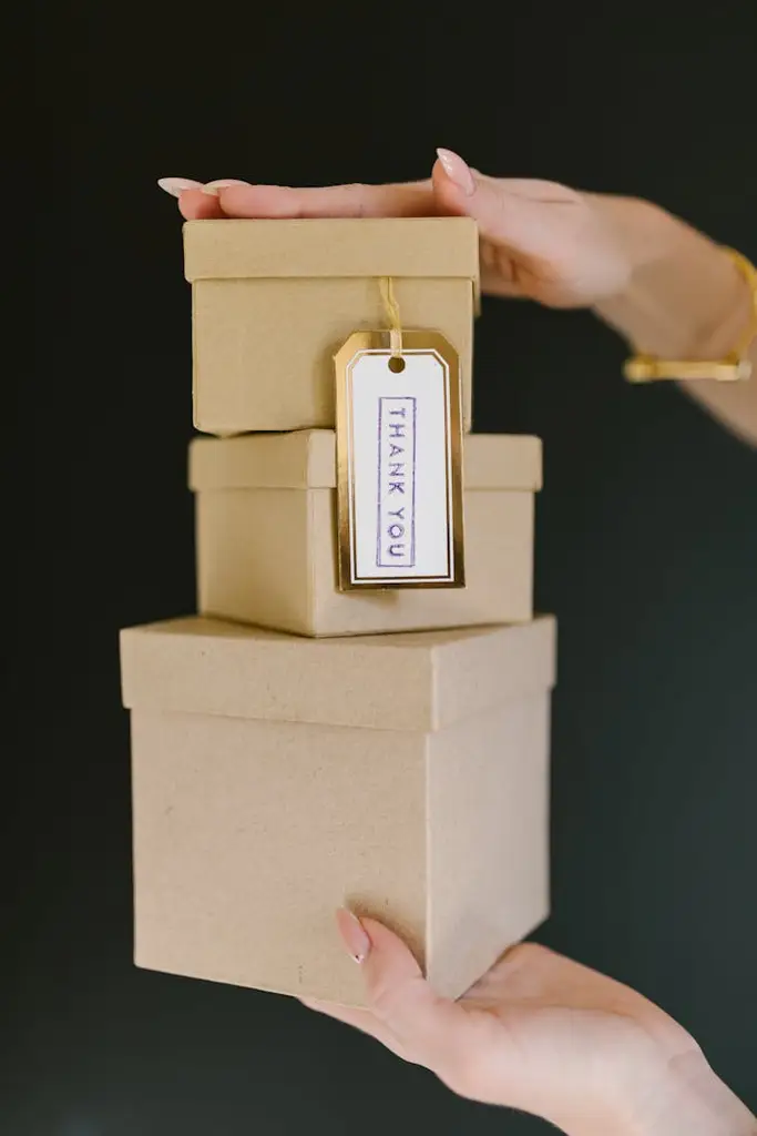 Three kraft gift boxes stacked with a 'Thank You' tag held by a woman's hands.